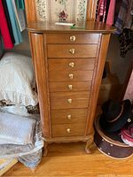 Front view of the tall wooden jewelry chest showing eight drawers with brass knobs and carved legs.