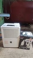 Photo showing white Kenmore dehumidifier and boxed UltiTechPro sump pump side by side in basement setting.