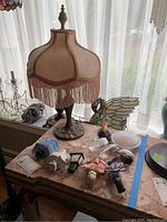 Full view of Victorian style table lamp with fringe shade and metal base on a marble top table with assorted night lights and parts around it.