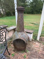 Front view of outdoor metal chiminea showing grapevine and leaf decorative embossing with mesh screen covering fire opening and rusty finish.