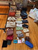 Full overview of all purses and bags arranged on wooden floor including large art print totes, clutch purses, coin purses, and wallets.