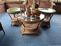Full view of the three rattan tables showing two smaller round tables and one larger oval coffee table with glass tops on a blue carpeted patio.