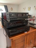 Stack of three stereo components from Technics, Onkyo, and Kenwood on a wooden surface in a living room setting.