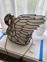 Photo of stained glass swan lamp showing side profile with wings spread, electrical cord visible
