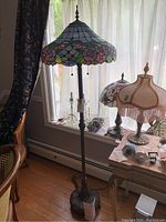 Full view of Tiffany style stained glass floor lamp standing beside a window and chairs.