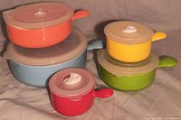 Photo of five colorful handled food storage containers stacked and arranged showing lids and colors