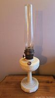 Full view of the antique Aladdin Model B oil lamp showing white alacite base with Lincoln drape pattern, brass burner, and tall glass chimney.
