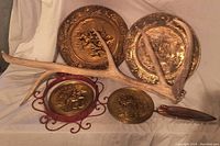 Overview of five items including four brass plates and a mounted antler incense holder lying on a fabric background