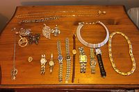 Full overview of assorted jewelry on wooden surface including necklaces, brooches, and wristwatches