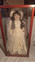 Front view of the porcelain Victorian bride doll inside a glass wooden display case.