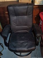 Front view of black synthetic leather chair showing padded armrests and cushioned backseat with wear.