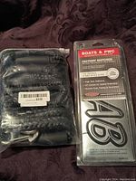 Photo shows packaged 4 ft bungee dock line in black with metal hooks alongside packaged registration number kit.