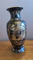 Black and gold vase with painted scenes on one side and detailed ornamental patterns on neck and base.