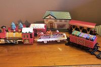 Red and gold locomotive and three rail cars arranged in sequence alongside a small model building with green roof.