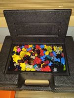 Open black plastic case filled with colorful Crazy Bones game pieces including yellow, red, blue, black, and translucent figures.
