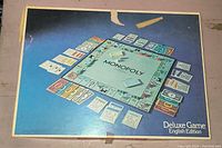 Game box lid showing Deluxe Monopoly board game's board with classic layout and money compartments.