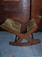 Side view of vintage wooden foot rocker showing the curved base and patterned upholstered seating area.