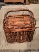 Woven wicker picnic basket with handle and hinged lid shown closed.