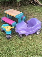 Photo of the Little Tikes kids picnic table with pink benches, purple ride-on car, and blue and yellow tricycle on grass.