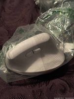 Top side view of the white ergonomic wireless mouse showing the side buttons and 'logi' branding, wrapped in clear plastic.