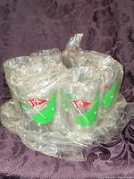 Set of several cups wrapped in plastic showing 19th hole golf flag design on green putting surface graphic.