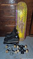 Photo showing men's black rollerblades, skateboard deck with worn yellow and purple honeycomb design, and two sets of skateboard trucks and wheels.