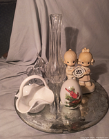 Overall view of all items in the lot placed on the etched mirror tray showing the Precious Moments figurine, glass vase, elephant paperweight, white ceramic dish, and cardinal egg.