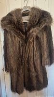Full view of the long fur coat hanging on a hanger, showing the full length and fur collar details.