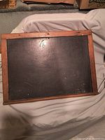 Full view of vintage chalkboard laid flat on cloth, showing wooden frame and ledge at the bottom.