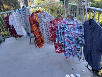 View of 11 men's Hawaiian-style short sleeve shirts with various colorful prints hanging on a clothesline outdoors.
