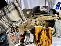 Photo of entire lot showing wool blanket, books, folding shovel, travel towel, cast iron pan, gloves, bag, and pants laid out