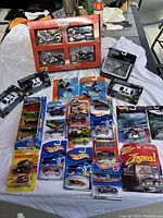 Wide angle image showing the entire lot on a white cloth backdrop with all vehicles in sealed packages or boxes, including the boxed motorcycle set and multiple blister packs.