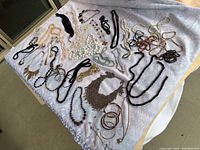 Overhead photo of assorted necklaces and bracelets arranged on white patterned cloth, showing variety in bead colors and necklace styles