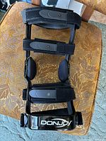 Top-down view of the Donjoy knee brace showing adjustable straps and hinge points, placed on a textured fabric chair.