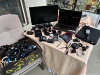 Wide overview of table showing laptop, monitor, headphones, power bank, calculator, metronome, rangefinder, phones and box of cables