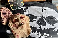 Wide shot showing two horror masks and boxed Halloween pumpkin string lights on a black and white skull bedspread.