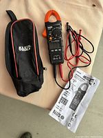 Photo showing the Klein Tools branded soft zippered carrying case, the CL210 clamp meter with test leads attached, and folded instruction manual.