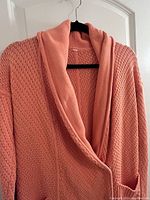 Front view of peachy coral knit cardigan on black hanger showing textured knits and shawl collar