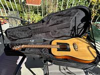 Oscar Schmidt acoustic guitar in black soft padded case, natural wood finish, black pickguard, shows wear.