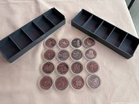 Collection of 15 commemorative Canada dollars in protective cases alongside 2 black display trays with separate compartments.