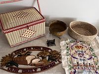 Woven sewing basket, wooden bowl, coiled basket, small metal sewing machine pencil sharpener, embroidered coronation cloth, and metal bread sign displayed together.