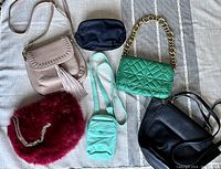 Overview photo showing all six handbags arranged on a neutral fabric background to illustrate the variety of colors, textures and styles in the lot.