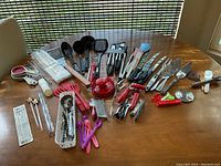 Wide view of assorted kitchen utensils spread on wooden table showing multiple types of tools and measuring cups
