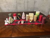 Wide view of all Christmas candles arranged on red and green plaid cloth on table.