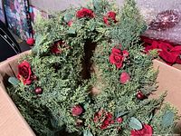 23-inch floral wreath with red roses, greenery, and small red ornaments inside a cardboard box.