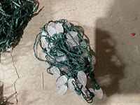 Clear leaf-shaped bulbs on green wired Christmas lights coiled on the floor