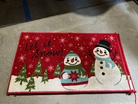 Photo of three red Christmas rugs featuring two snowmen, green pine trees, snow flakes, and 'Let it snow!' text