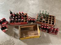 Overview of Coca-Cola collectible bottles and wooden carriers, showing full and empty glass bottles in crates and loose on floor.