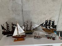 Wide view showing all six ship models arranged on a table against a concrete wall.