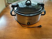 Angled front view of stainless steel Crock-Pot slow cooker showing control dial and power cord on wooden table.